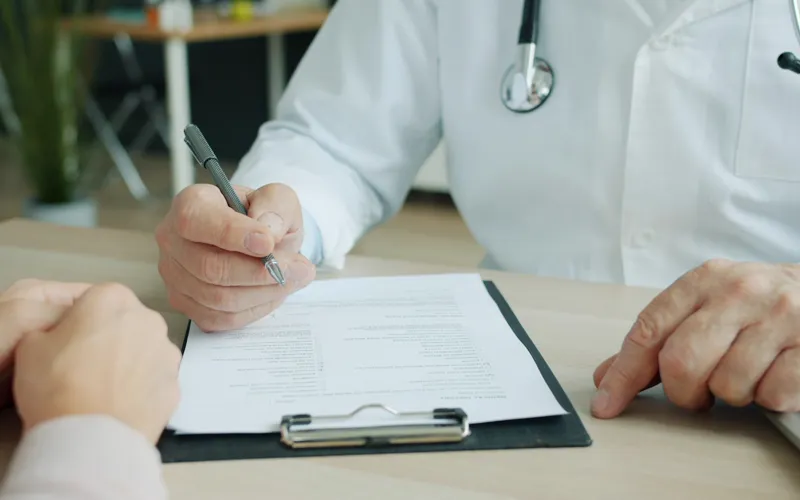 Médico cumplimentando un impreso durante la consulta con un paciente